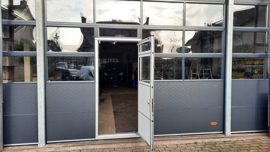 Geöffnete Schlupftür in einem anthrazit farbenen Compact Tor mit Fenstern